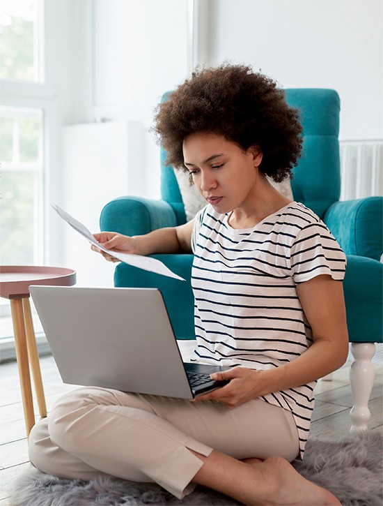 Woman sitting on floor with laptop on lap and a paper in hand